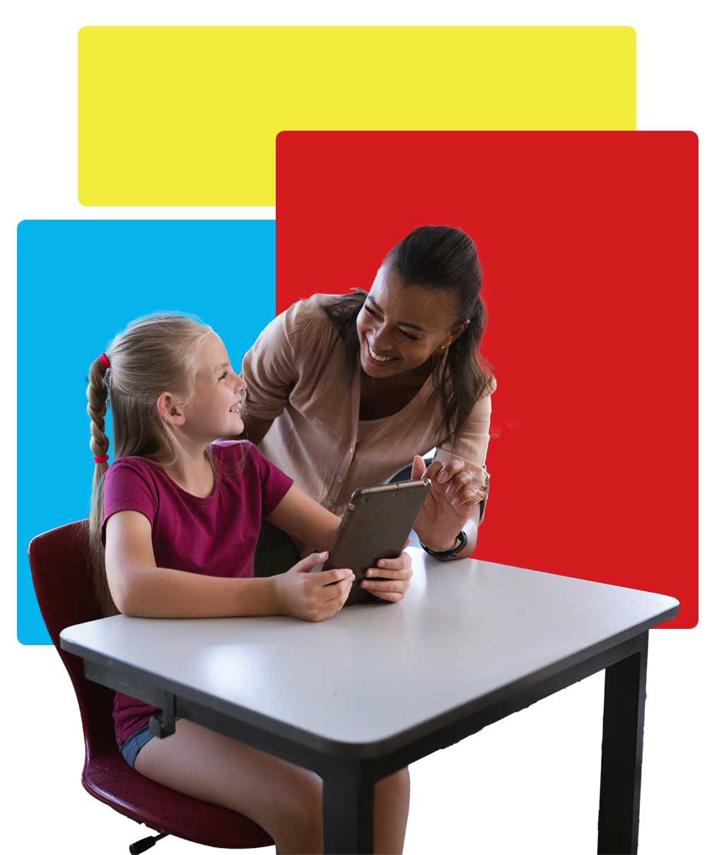 Smiling therapist sitting beside a young girl holding a tablet at a classroom desk, engaging in interactive learning.